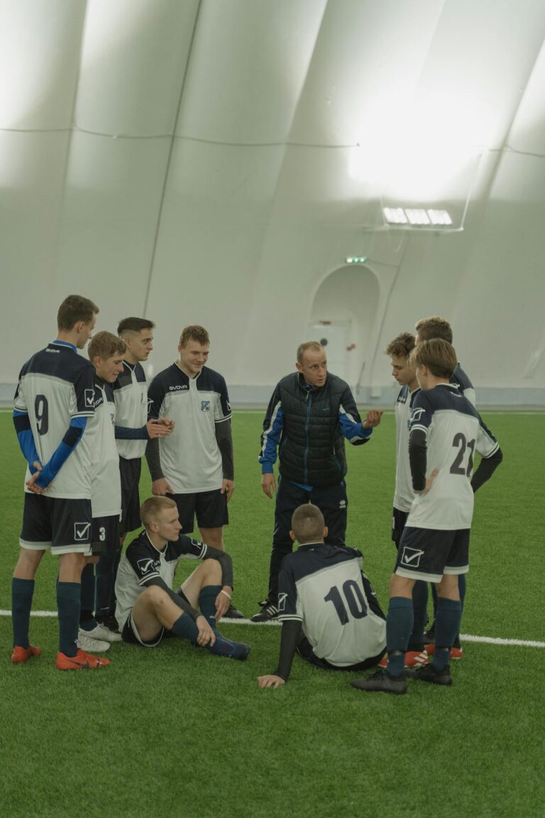 Coach giving instructions to a young soccer team inside a sports facility.