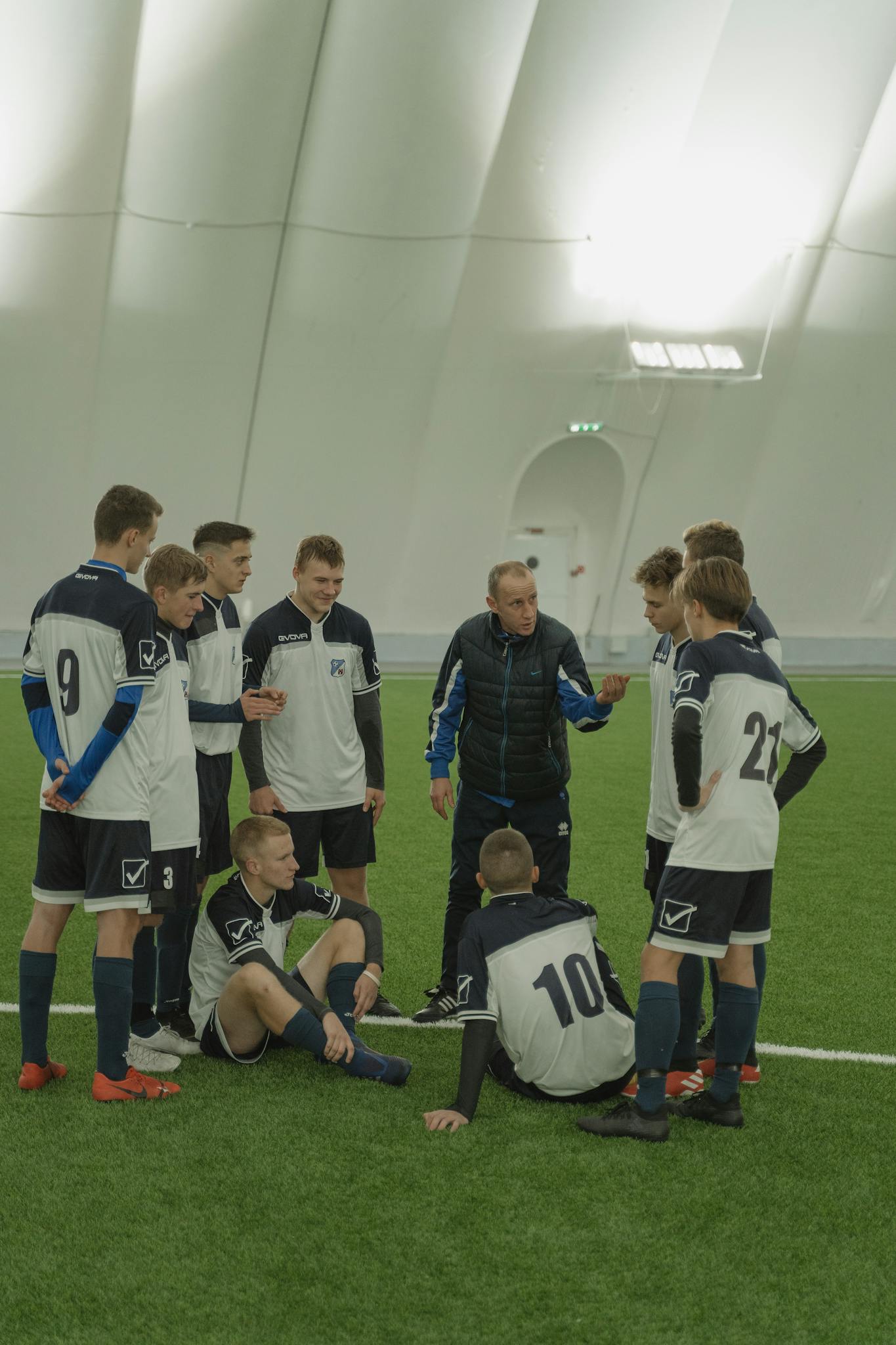 Coach giving instructions to a young soccer team inside a sports facility.