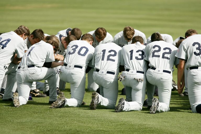 Group of baseball players in uniforms kneeling together on a sports field.